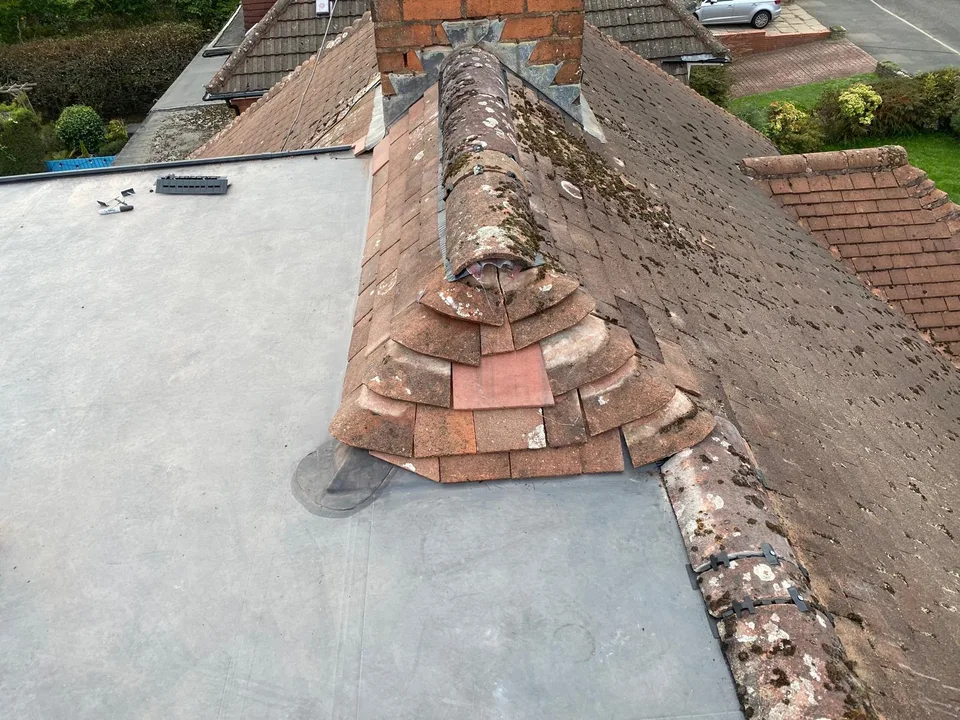 Flat roof covering meeting tiled roof slopes beside a chimney